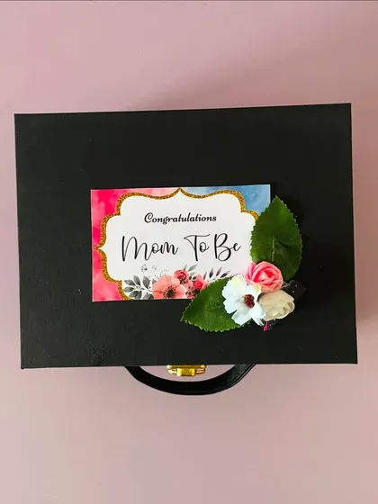 A closed view of the "Mom To Be" hamper, showing the custom tag on the black suitcase box. The presentation is just as important as the gifts inside.