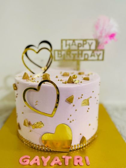 A sweet pink cake decorated with golden hearts and gold leaf, perfect for celebrating someone you love.