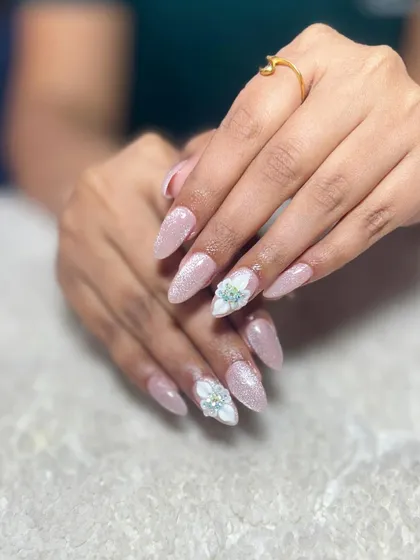 A delicate and feminine design. These glittery pink almond nails are accented with 3D flowers made of sparkling white crystals.