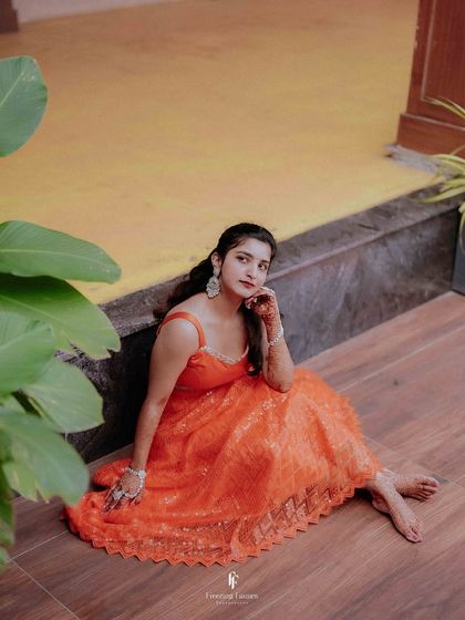 A lovely portrait of the bride seated on the floor in her bright orange dress during her Haldi ceremony, looking calm and beautiful.