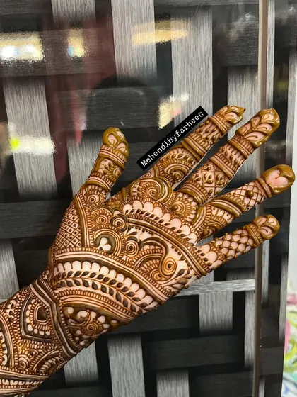 A classic Indo-Arabic design shown here with fresh henna paste. The pattern features bold outlines and fine, detailed fillings, covering the back of the hand beautifully.
