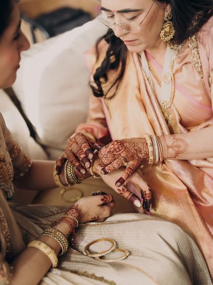 An intimate moment of a mother helping her daughter with her bangles. These quiet, behind-the-scenes interactions are what make a wedding so special, and we ensure the outfits are perfect for them.