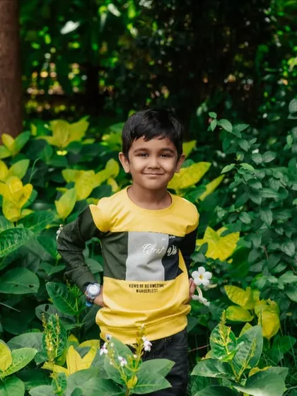 A confident pose amidst the greenery. This outdoor kids' portrait showcases a natural smile and relaxed attitude.