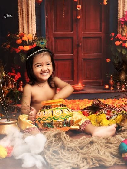 Celebrating Janmashtami with an adorable 'Little Krishna' shoot. This toddler is having fun playing with a pot of 'butter' in a vibrant, traditional setup.