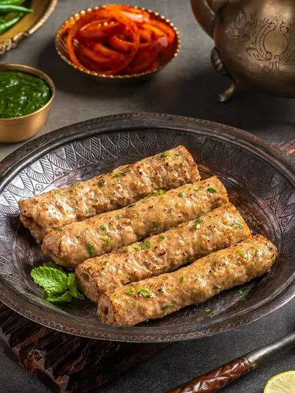Chicken Seekh Kebab on a rustic platter. The image for The Mughal House is styled with fresh mint and onions to suggest authentic flavors.