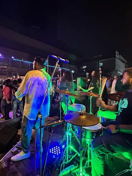 A shot from behind the drum kit, capturing the band and the dancing crowd at the Arihant Superstructures event.