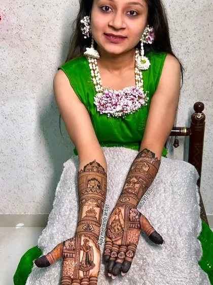 A happy bride showing off her portrait mehndi. The design features the bride and groom on her palms, with intricate patterns extending up her arms.