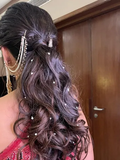 A soft, curly ponytail accessorized with a pearl hair chain. This is a romantic and elegant choice for a sangeet or reception.
