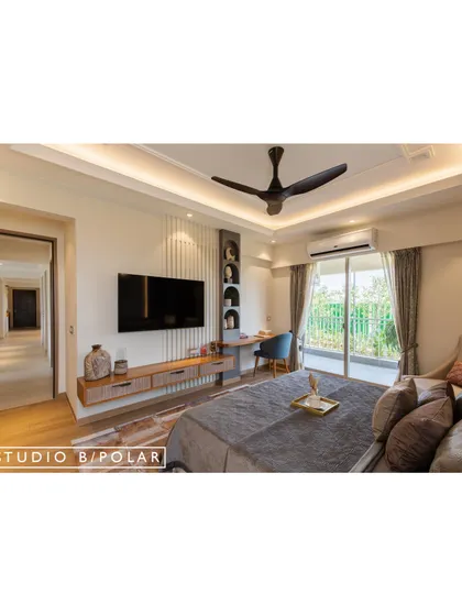 The TV wall in the same bedroom integrates a floating console with a study desk, creating a functional and seamless unit. Arched niches add a soft, sculptural element to the storage.