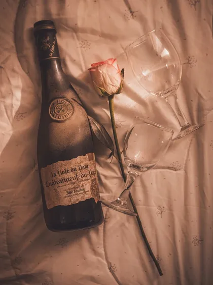 A moody, romantic flat lay of a wine bottle and glasses on a soft blanket, creating a cozy and intimate "night in" feeling.