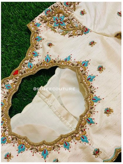 The back of the cream blouse, featuring a round keyhole cutout. The border of the cutout is finished with the same intricate floral embroidery seen on the sleeves.