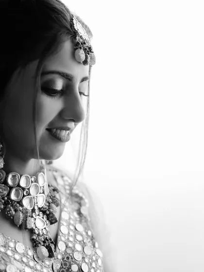 A moment of quiet joy captured in classic black and white. This portrait highlights the bride's beautiful smile and the intricate details of her mirror-work jewelry, creating a timeless and artistic image.