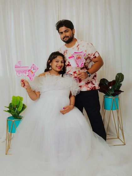 A classic white ruffled gown is a timeless choice for a maternity shoot. Here, the couple uses "It's a Girl" props to make a fun and exciting announcement.
