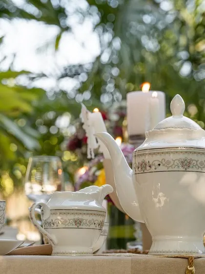 An elegant outdoor tea party setting for Vigneto's crockery. This lifestyle shot uses natural light and a lush green background to create an aspirational scene, showing how the dinnerware can elevate an everyday moment into a special occasion.