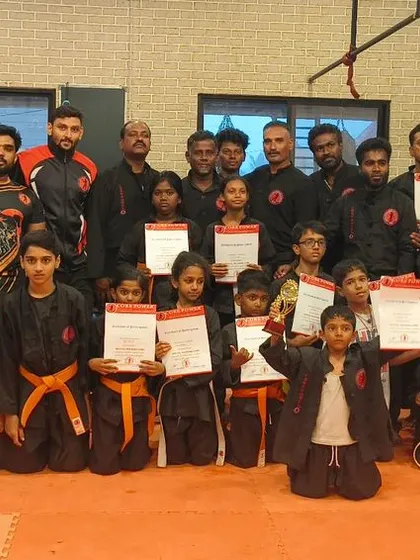 A proud group of students, both children and adults, holding up their new certificates after a successful belt grading.
