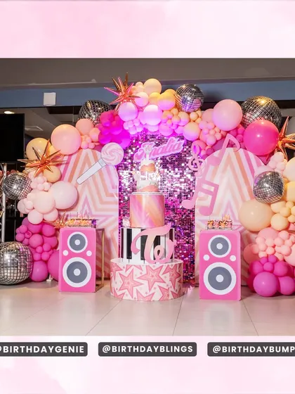 A rockstar-themed 16th birthday party with a pink shimmer wall. The setup includes speaker props, a microphone, and disco balls to create a full concert-stage feel.