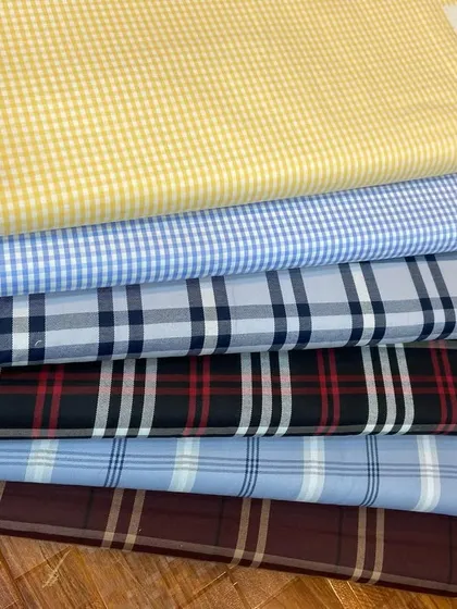 A selection of my premium cotton fabrics for custom shirts. This stack includes classic gingham, tartan, and other check patterns in various colors.