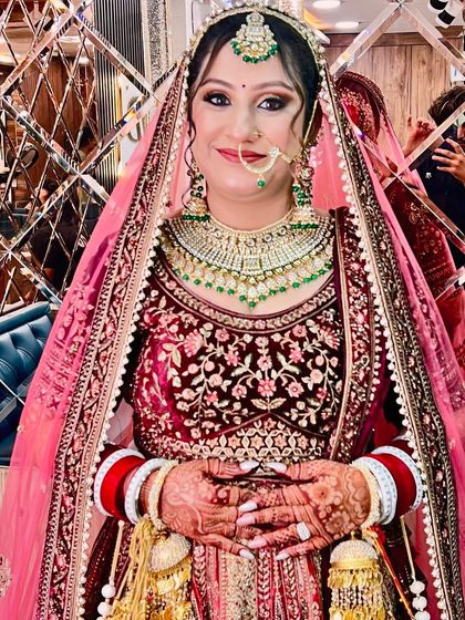 This bride is glowing in a deep maroon velvet lehenga. We created a classic bridal makeup look with smoky eyes and a flawless base, complemented by a beautiful nath and layered necklaces.