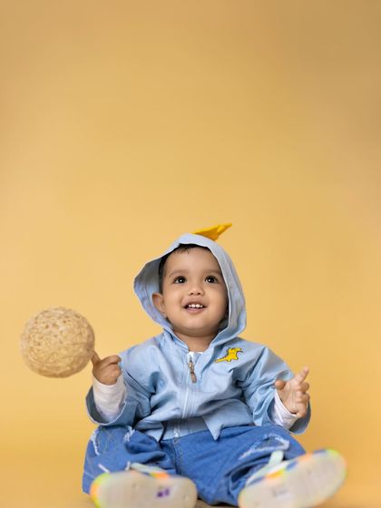 A happy toddler sits on a yellow background, holding a textured ball and smiling brightly. This image is full of life and captures the simple joy of playtime.