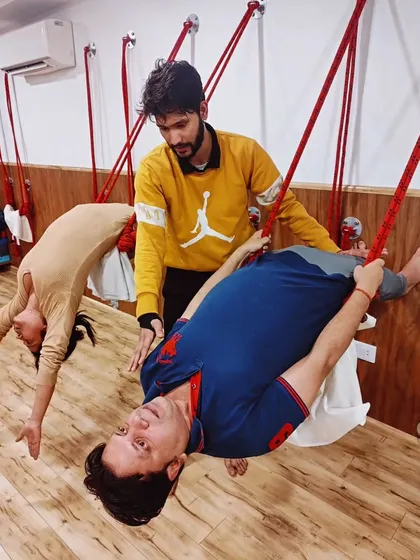 A student hangs in a supported inversion using the wall ropes, allowing the spine to lengthen and release tension. This is a deeply therapeutic and restorative practice.