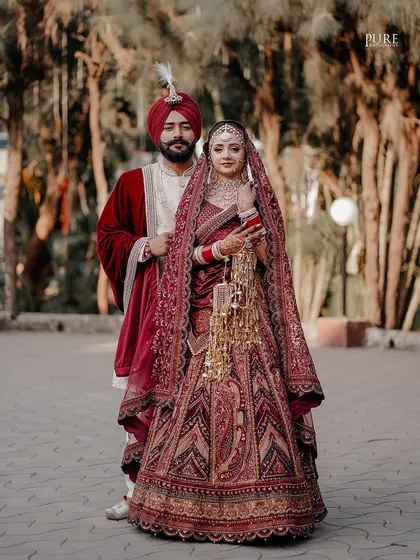 A classic wedding portrait where the bride and groom stand together, showcasing their magnificent wedding attire and the bride's beautiful kaleere.