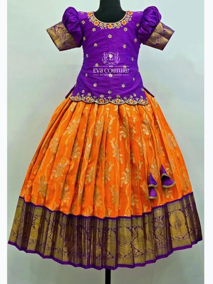 A vibrant orange and purple Banarasi lehenga. The blouse features floral embroidery, and the skirt has a beautiful brocade pattern.