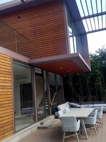 A daytime view of our modern villa project highlights the clean lines and material palette. The combination of wood cladding, a robust steel pergola, and an expansive deck creates a functional and elegant outdoor living area.