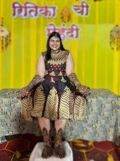 A full-length shot of a bride at her mehendi ceremony, showcasing her intricate henna on both her hands and feet.