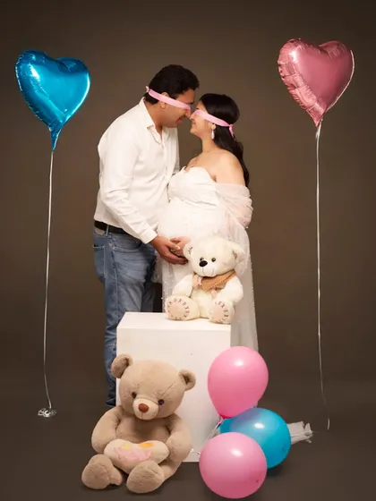 A playful and sweet gender reveal concept. The blindfolded couple, surrounded by pink and blue balloons and teddy bears, builds anticipation for the big surprise.