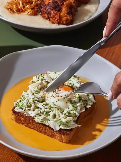 A guest cutting into the Warm Crab Toast, breaking the yolk of the slow-cooked egg to enrich the prawn bisque.