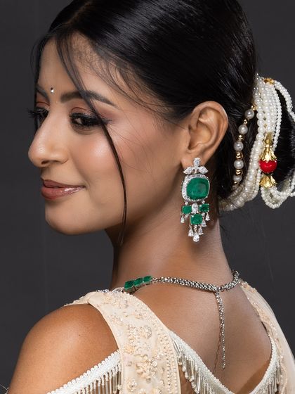 A profile shot of a model, focusing on her traditional Indian hairstyle and emerald earring.