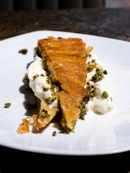 A slice of baklava served with Turkish ice cream, captured in beautiful natural sunlight. The light creates highlights and shadows that emphasize the flaky texture.