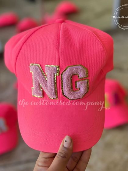 A closer look at our personalized neon pink caps. The chenille initial patches add a fun, textural element, making them a stylish and eye-catching accessory.