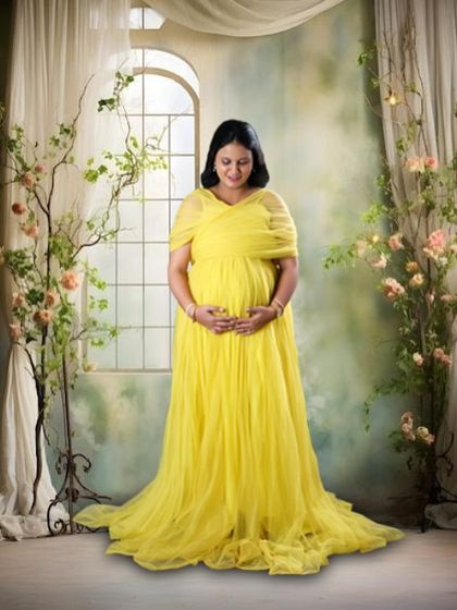 This full-length shot in a studio setting showcases the beautiful flow of the yellow maternity gown. The elegant backdrop complements the dress perfectly.