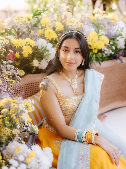 A dreamy, sun-kissed Mehendi look. The bride is surrounded by flowers, and her makeup is kept soft and natural to match the ethereal, golden-hour vibe.