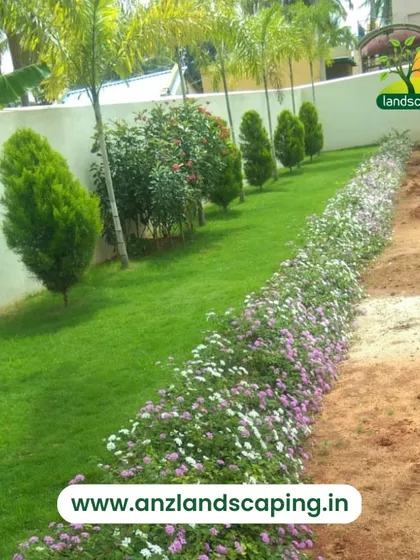 A well-maintained garden path bordered by a line of flowering shrubs on one side and a healthy lawn with palm trees on the other, showcasing a classic and clean landscape design.