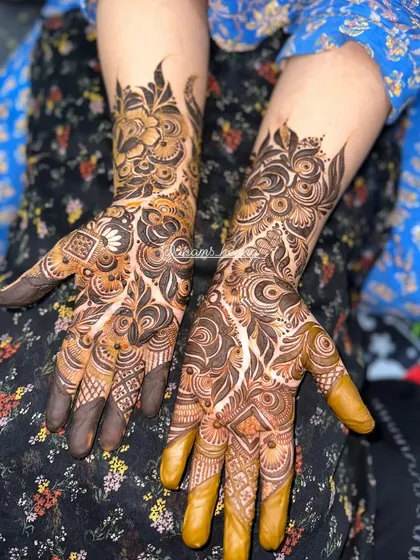 Both hands adorned with heavy, intricate bridal mehndi. The design covers every part of the hand and extends up the arm for a complete look.