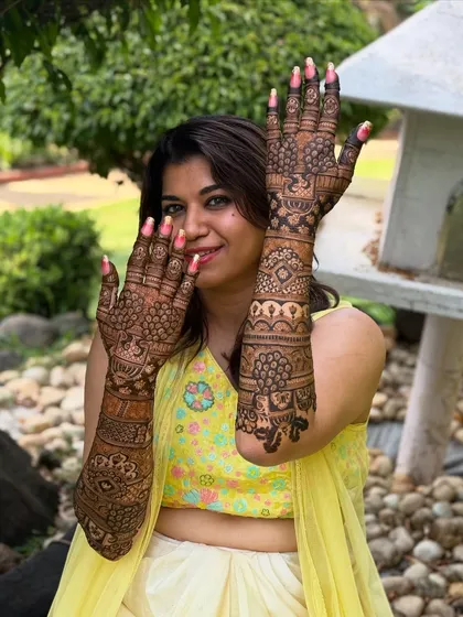 A happy bride posing outdoors, her intricate mehendi complementing her festive attire.