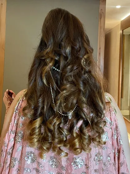 A beautiful view of this half-up, half-down hairstyle. The hair is styled in defined, bouncy curls with a delicate pearl chain accessory for a touch of elegance.