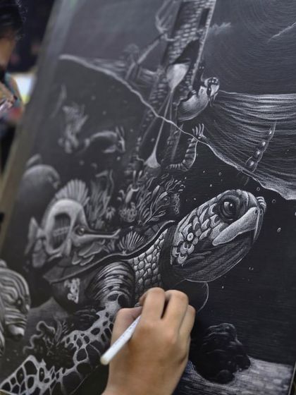 An over-the-shoulder view of the artist at work, showing the careful process of building up layers of white to create depth and form in her underwater drawing.