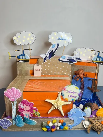 For Isha Ambani Piramal's twins, I created a magical 'land, air, and sea' themed hamper. This side shows the 'air' theme for Krishna, with planes and helicopters, and the 'sea' theme for Aadiya Shakti, with mermaids and shells.