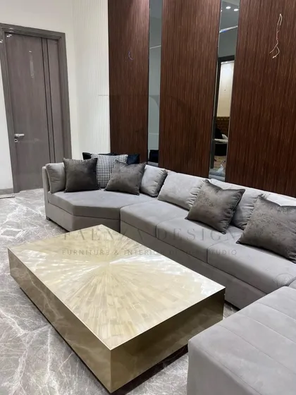 This large, grey L-shaped sectional provides ample seating for a family room. It is paired with a striking center table made of selenite with a brass base, blending comfort with high-end materials.