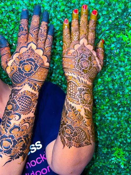 A vibrant and bold semi-bridal design. The contrast between the dark henna and the bright green background makes the floral patterns pop.