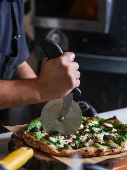Getting the perfect slice. Our pizzaiolo carefully cuts the Mushroom & Burrata pizza, ensuring every piece has the right balance of toppings and that amazing spinach cream sauce.
