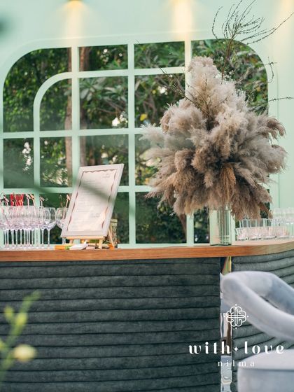 The custom-built bar from 'The Conservatory' baby shower. The rounded counter is wrapped in green suede fabric, topped with wood, and set against a window-paneled backdrop, making it a stylish focal point.