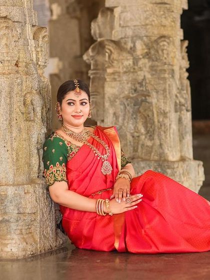 A serene portrait of a bride seated on the temple floor, surrounded by massive stone pillars. The scale of the architecture adds a sense of grandeur to the image.