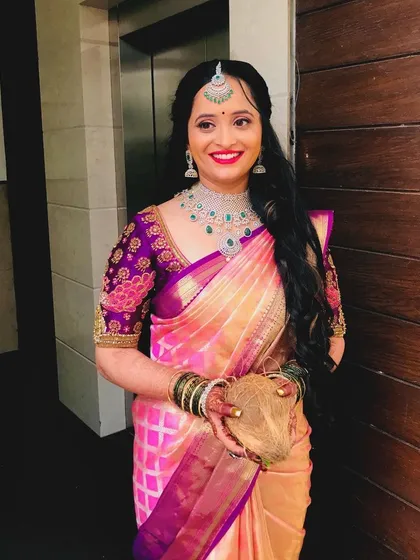 A happy, smiling bride holding a coconut, a traditional element of the Varapooje. Her makeup is bright and joyful.
