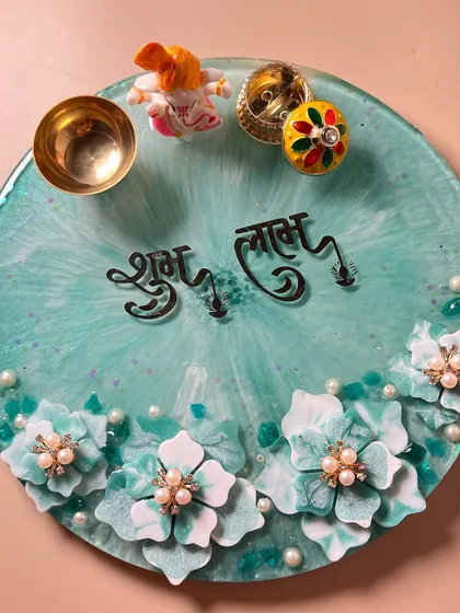 Bring a touch of handmade beauty to your prayers. This is a custom 10-inch resin pooja thali in a lovely sea-green shade, decorated with handcrafted flowers and pearls. It comes with a matching diya, Ganesh idol, and a small bowl for offerings.