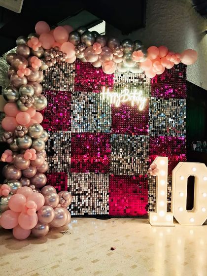 A sparkling 10th birthday setup. This decor features a pink and silver checkered sequin wall, a "Happy Birthday" neon sign, and large marquee numbers, creating a fun and glamorous photo corner for the birthday girl.