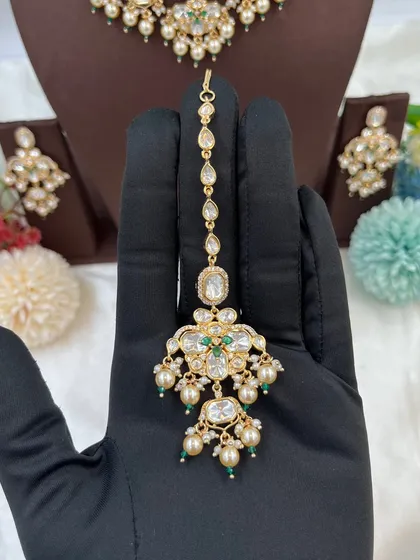 A close-up of the 'Noor Nazaakat' maang tikka, featuring moissanite, kundan, and delicate pearl drops.